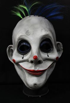 a creepy clown mask with green hair and blue eyes is shown in front of a black background