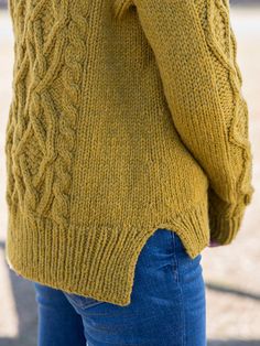 a woman wearing a yellow sweater and blue jeans is talking on her cell phone while walking down the street