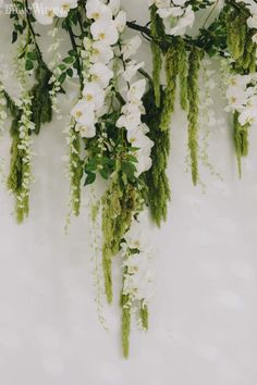 white flowers and greenery are hanging on the wall