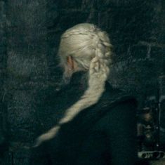 a woman with white hair and braids in a black jacket is standing next to a brick wall