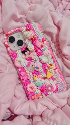 an iphone case with hello kitty on it laying on a pink bed sheet and blanket