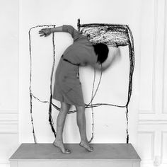 a black and white photo of a woman leaning on a piece of art with her hands in the air