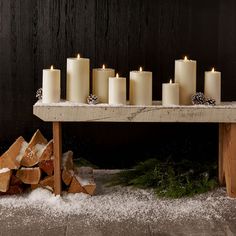 lit candles sit on a table with snow around it and logs in front of them