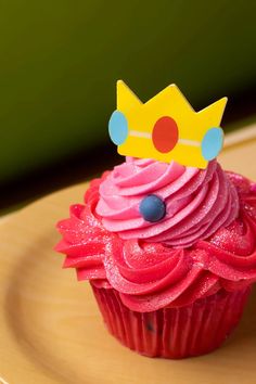 a cupcake with pink frosting and a crown on top is sitting on a plate