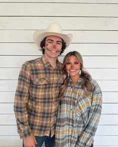 a man and woman standing next to each other in front of a white wall wearing cowboy hats