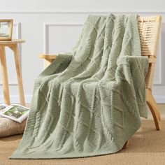 a green blanket sitting on top of a wooden chair next to a table with a magazine