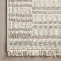 a white rug with fringes on the bottom and side, in front of a beige wall