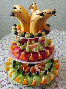 three tiered fruit tray with bananas, grapes and oranges in them on a table