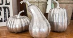 three silver pumpkins sitting on top of a wooden table