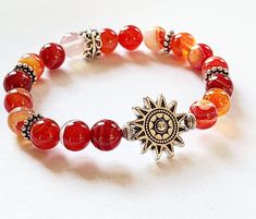 SUNFIRE Bracelet by Evil Queen Jewelry Natural Banded Agate in Sunset Fire Colors, Red Orange, a yellow and White Antique Silver Sun is the focal with antique Silver Accent Beads. Polished, Smooth, Natural Stone Stretch Bracelet measuring approximately 7 inches with 8mm round stones If you need a different length, please contact me! Each Stone is Unique and made by nature, no two are alike As with all jewelry, wear with care. Stones and metal do not always do well with chemicals or water. Best t Fire Bracelet, Orange Accessories, Fire Jewelry, Autumn Bracelet, Queen Jewelry, Orange Bracelet, Sun Stone, Orange Crystals, Red Sun