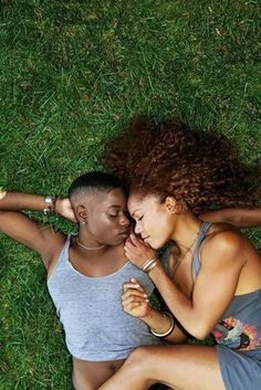 two people laying in the grass talking on their cell phones and looking at each other