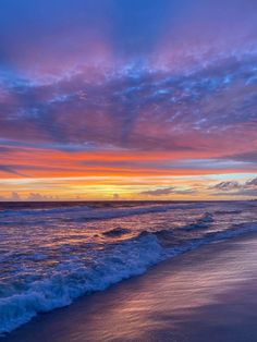 the sun is setting over the ocean with clouds in the sky and waves on the beach