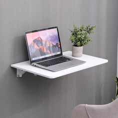 a laptop computer sitting on top of a white shelf next to a potted plant