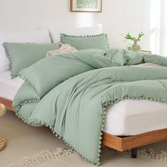 a bed with green comforter and pillows in a white room next to a window