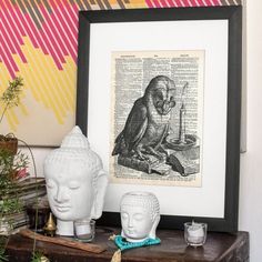 an owl sitting on top of a table next to two buddha heads and a framed print