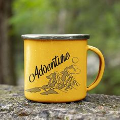 a yellow coffee mug with the words adventure on it sitting on top of a rock