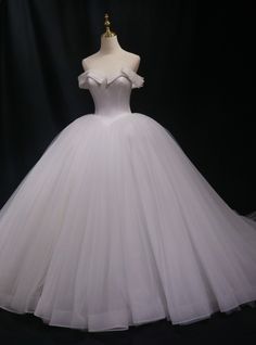 a white ball gown on display in front of a black background with the dress off to the side