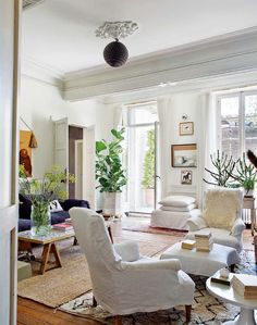 a living room filled with lots of white furniture and plants on top of the tables