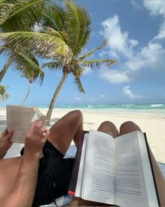 a man reading a book under a palm tree on the beach