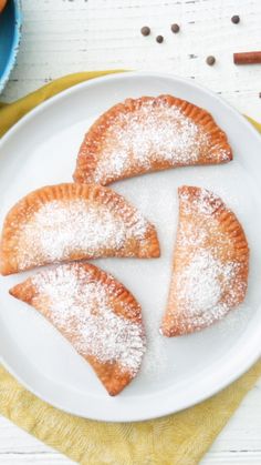 three pastries on a plate with powdered sugar and cinnamon sticks in the background