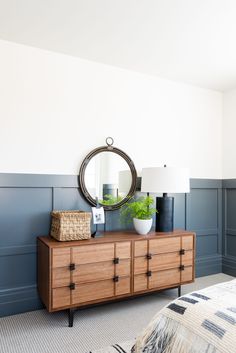 a dresser with a mirror and lamp on it in front of a blue painted wall