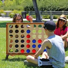 two girls and a boy playing giant connect game in the grass with an adult woman