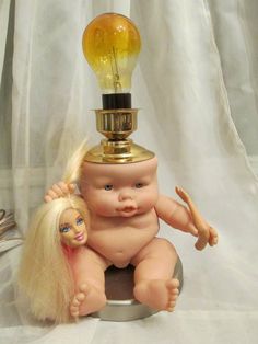 a baby doll sitting on top of a table next to a light bulb with a long blonde hair