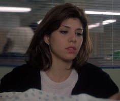 a woman sitting in front of a window looking down at something on the table behind her