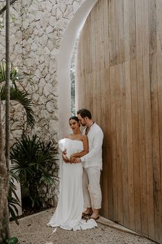 a man and woman standing next to each other in front of a wooden wall with an arch