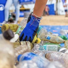 a person wearing blue gloves standing on top of a pile of plastic bottles and trash