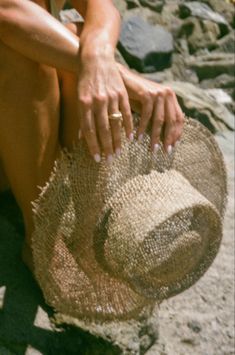 a woman sitting on top of a sandy beach next to a large brown straw hat