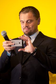 a man in a suit holding a microphone and taking a photo with his cell phone