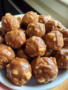 a plate filled with chocolate covered donuts on top of a wooden table next to a window