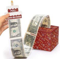 a hand holding a roll of money with a happy birthday candle on top of it