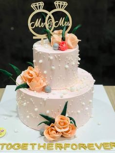 two tiered wedding cake with flowers on the top and initials on the side, sitting on a table