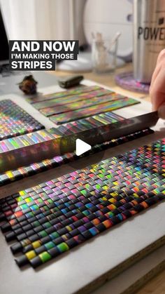 a person is holding a pair of scissors in front of some colored squares on a table