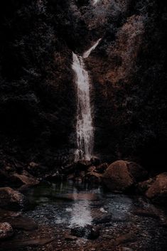 a waterfall in the middle of a forest with rocks and water flowing from it's sides