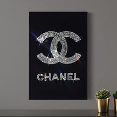 a chanel poster on a wall next to two potted plants and a gold planter