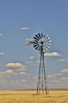 a windmill in the middle of an open field with blue sky and clouds behind it