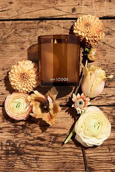 an arrangement of flowers and a perfume bottle sitting on a wooden surface with the word new lodge written in it