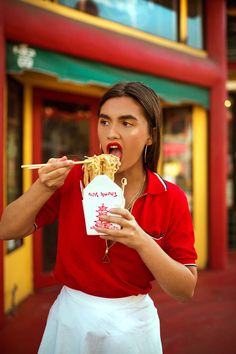 a woman in red shirt eating food with chopsticks