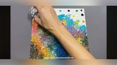 someone is painting on a piece of paper with colorful paint and silver foil sprinkles