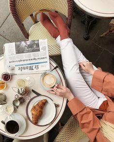 a woman is sitting at a table with her feet up on the table while reading a newspaper