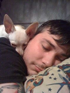 a man laying in bed with his head on the pillow next to a small dog