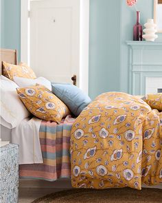 a bed with yellow and blue comforters on top of it in a bedroom next to a fireplace