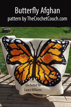 A vibrant, single crochet afghan featuring a detailed monarch butterfly design drapes gracefully over an outdoor deck railing. The bright orange and black butterfly contrasts beautifully against the natural wood Crochet Butterfly Blanket Pattern, April Butterfly, Butterfly Afghan, Yarn Bobbins, Tunisian Simple Stitch, Butterfly Blanket, Crochet Pattern Written, Butterfly Monarch, Crochet Critters