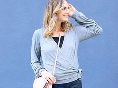 a woman in jeans and a gray sweater is talking on her cell phone while holding a pink purse