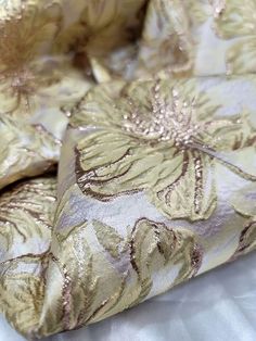 the fabric is gold and white with large flowers on it's side, as well as metallic foil