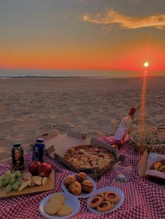 a picnic on the beach at sunset with pizza, fruit and beer in front of it