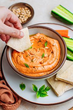 a hand dipping a piece of pita bread into a bowl of hummush